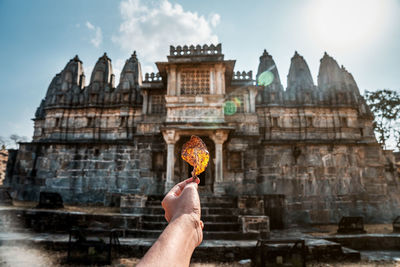 Hand holding autumn leaf against building