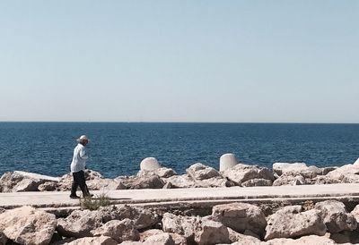 Rear view of man standing by sea against clear sky