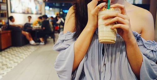 Midsection of woman having drink while standing at cafe