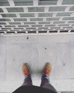 Low section of man standing by wall on sidewalk