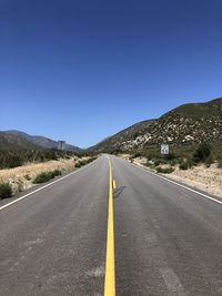 Road leading to mountains against clear blue sky