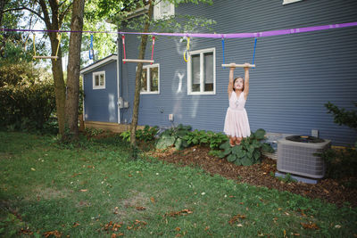 A little girl in a pink dress hangs from a bar swinging outside