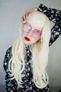 Woman with long blond hair wearing purple sunglasses against wall