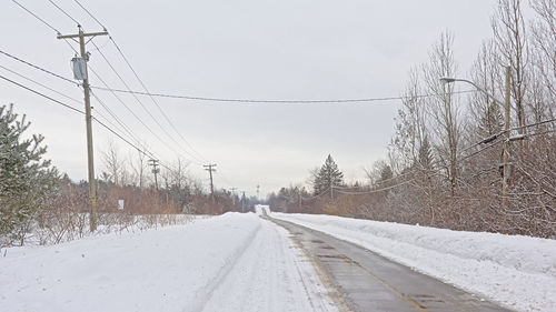 Snow covered electricity pylon against sky during winter
