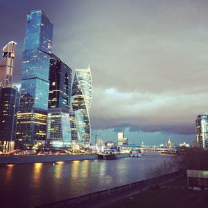 Illuminated buildings by river against sky in city
