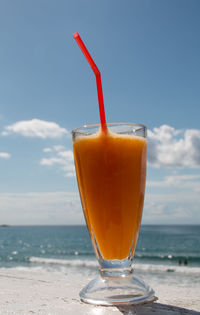 Close-up of drink on table at beach against sky