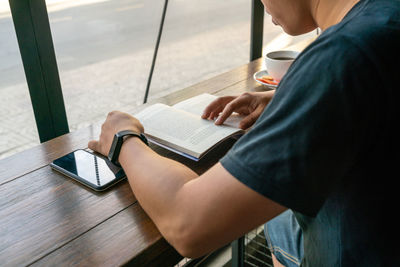 Midsection of man reading book at cafe