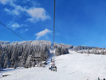 Ski lift by snowcapped mountains against blue sky