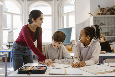 Happy teacher looking at female student while assisting in classroom