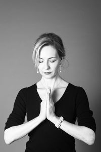 Woman with hands clasped standing against gray background