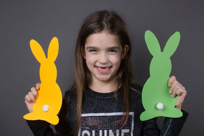 Portrait of smiling girl holding paper eater bunny against gray background