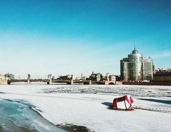 View of buildings on snow covered land against blue sky