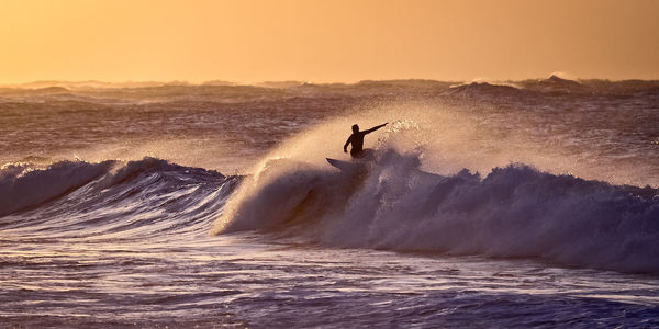 Silhouette man surfing in sea against sky during sunset