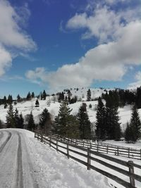 Road by snow covered landscape against sky