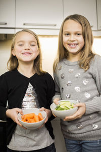 Portrait of happy sisters holding sliced vegetables in bowls at home