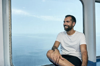 Man sitting by sea against sky