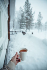 Midsection of woman holding tea cup against snow