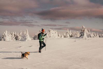 Side view of woman with dog hiking on snow