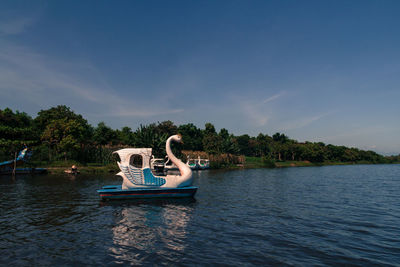 Swan shaped pedal boat moored at lake against blue sky