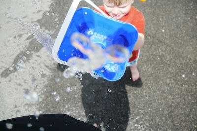 High angle view of boy playing with water while standing on street during summer