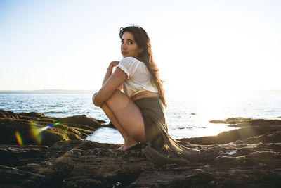 Young woman on rock at beach against sky