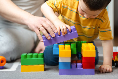 A three year old toddler boy plays with his dad with a construction set in the children's room.