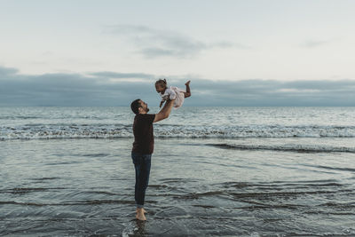 Dad throwing his daughter in air in the ocean negative space