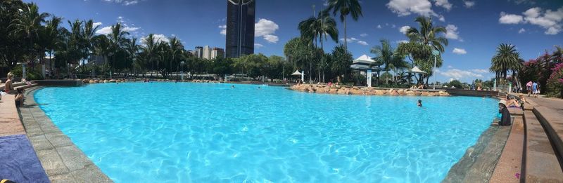 Swimming pool by palm trees against sky