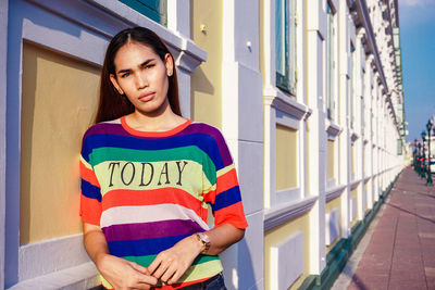 Portrait of young woman standing against wall