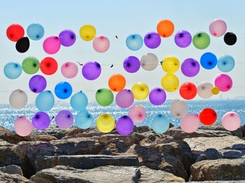 Multi colored balloons on rock by sea against sky