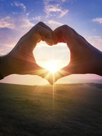 Two adult hands forming a heart shape against a sunset