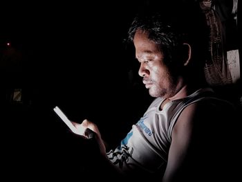 Side view of young man using phone against black background