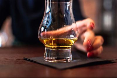 Midsection of woman having whiskey at table in bar