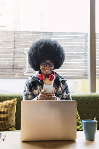 Businesswoman using smart phone sitting with laptop on table in coffee shop