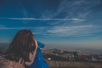 Rear view of woman photographing cityscape against blue sky