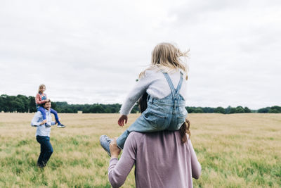 Parents carrying daughters while playing at meadow