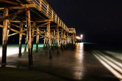 Illuminated pier over sea against sky at night