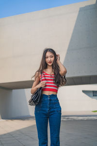 Portrait of young woman standing against wall