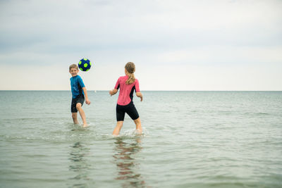 Playful friends playing with soccer ball in sea