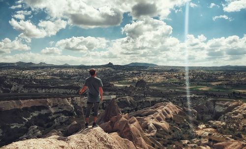 Rear view of man standing on rock while looking at landscape against sky