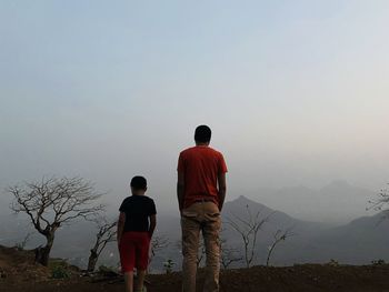 Rear view of men standing on mountain against sky