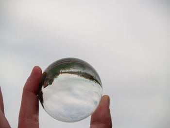 Close-up of hand holding glass against sky