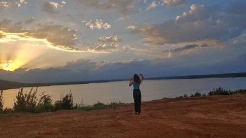 Rear view of woman standing against sky during sunset