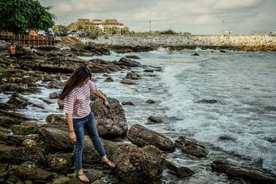 Rear view of woman standing on rock by sea