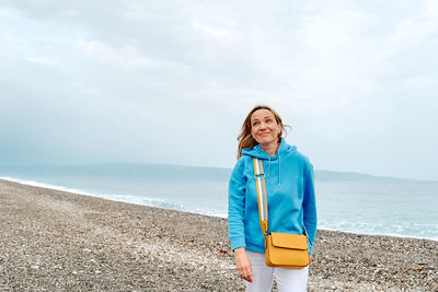 Young woman standing at beach against sky