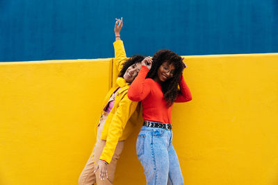 Smiling female friends dancing against wall