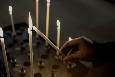 Cropped hand of woman igniting candle in darkroom