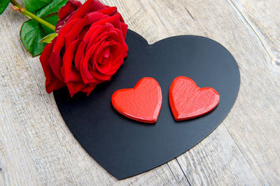 High angle view of red rose on heart shape at wooden table