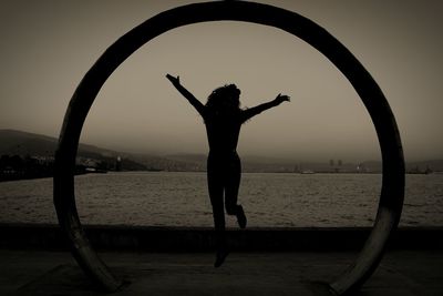 Silhouette woman jumping on promenade by sea against sky seen from circle