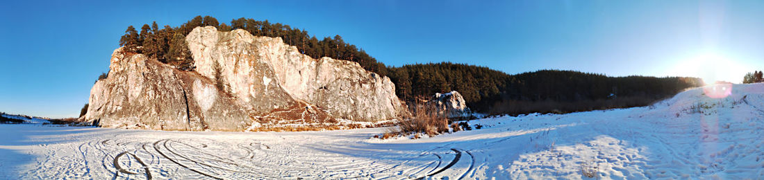 Winter mountain landscape, panoramic view of cliffs on frozen snow-covered river against blue sky